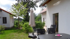 Un patio con una mesa, sillas y una sombrilla, además de un pequeño jardín.