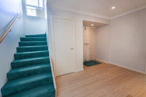 A staircase with teal carpet leading to a white door, a wooden floor, and a small window above the door.