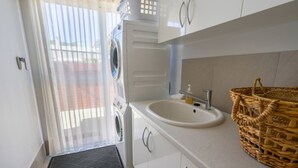 A laundry room with a washing machine, a sink, and a wicker basket. - West Beach House in West Beach (Esperance)