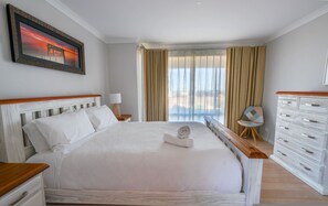 Een hotelkamer met een groot bed, een nachtkastje, een stoel, een dressoir en een raam met gordijnen.