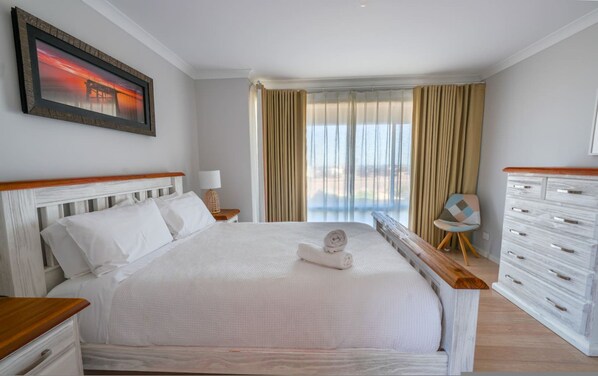 A hotel room with a large bed, a nightstand, a chair, a dresser, and a window with curtains.