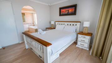Un dormitorio con cama de madera, mesitas de noche blancas, una lámpara de noche y un cuadro en la pared.