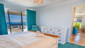 A bedroom with a large bed, a dresser, and a view of the sea through a sliding door. - West Beach House in West Beach (Esperance)