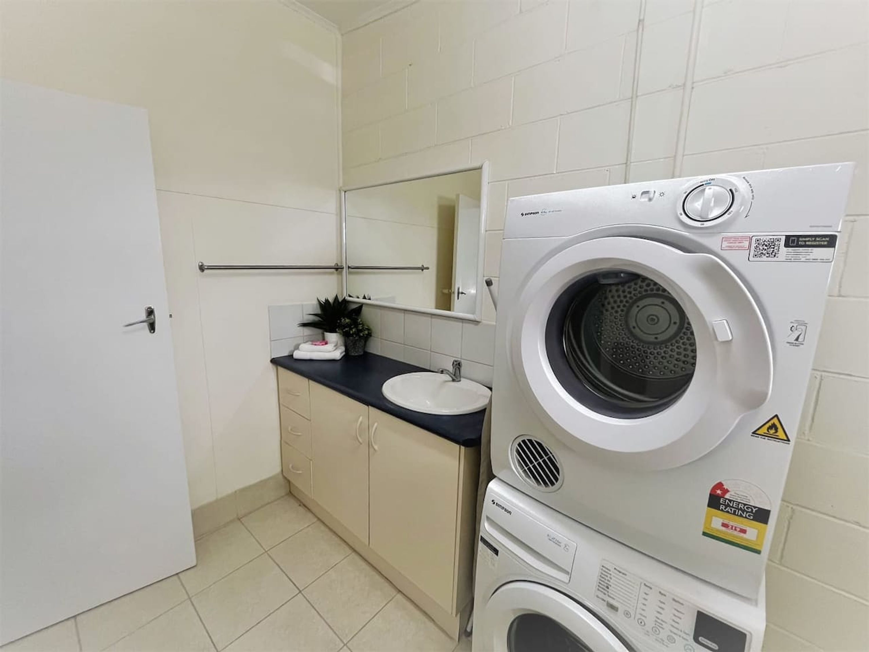 Ein kleines, modernes Badezimmer mit integrierter Waschmaschine und Trockner, einem Waschbecken und einem Spiegel.