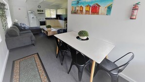 A compact living space with a kitchenette, a dining area with a table and chairs, a sofa, and a painting of colorful houses on the wall. - Esperance Little Units 1 (Esperance)
