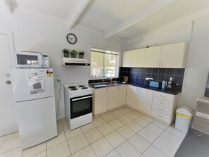 A compact kitchen with white cabinets, a stove, a microwave, and a sink. - Esperance Little Units 1 (Esperance)