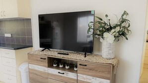 A modern kitchen with a flat-screen TV on a wooden cabinet, a small potted plant, and a trash bin. - Esperance Little Units 1 (Esperance)