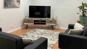 Un salon équipé d’un téléviseur à écran plat, de deux canapés, d’une table basse, d’un tableau accroché au mur et d’une plante en pot.