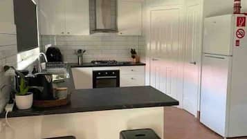 A modern kitchen with white cabinets, a black countertop, and two black stools.