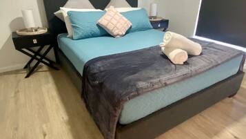 A bed with a dark headboard, a teal bedspread, and a rolled towel on the footboard.