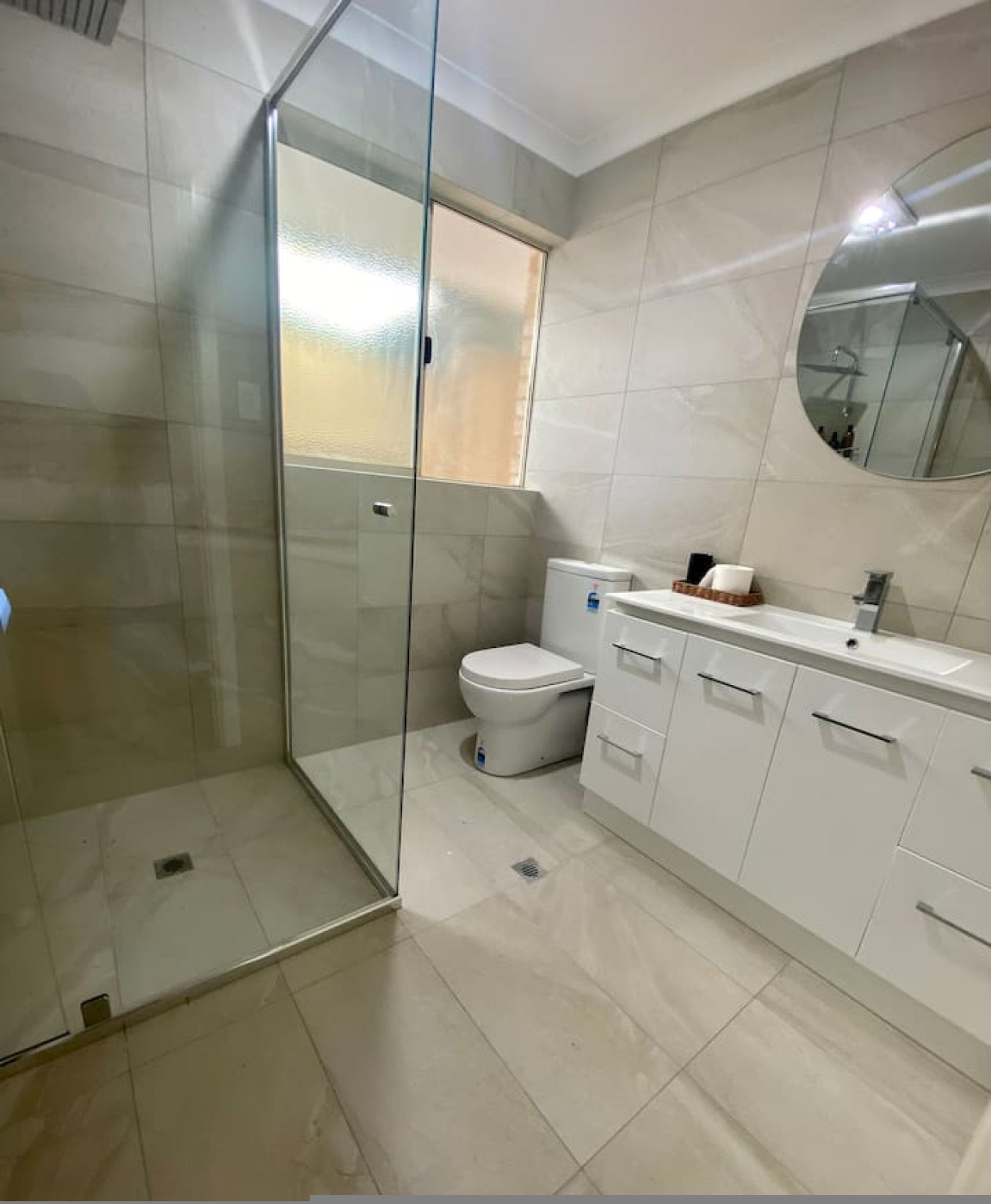 A bathroom with a glass-enclosed shower, a toilet, and a sink with a mirror above it.