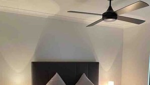 Une chambre à coucher avec un lit, un ventilateur de plafond, des lampes de chevet et une table de chevet.