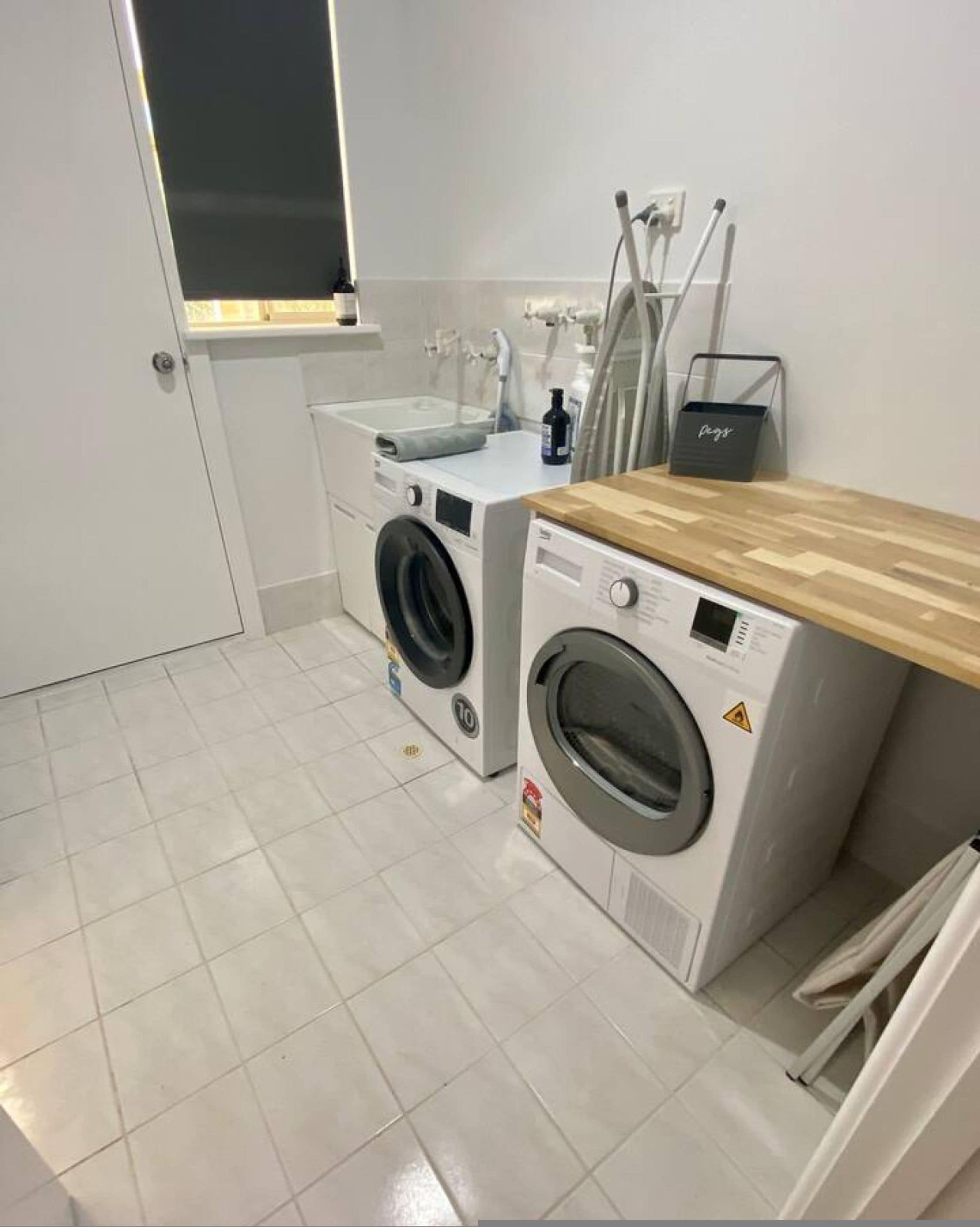 A laundry room with two washing machines, a sink, and a wooden countertop.