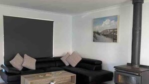 Un salon comprenant un canapé noir, une table basse en bois, une cheminée noire et un tableau accroché au mur.