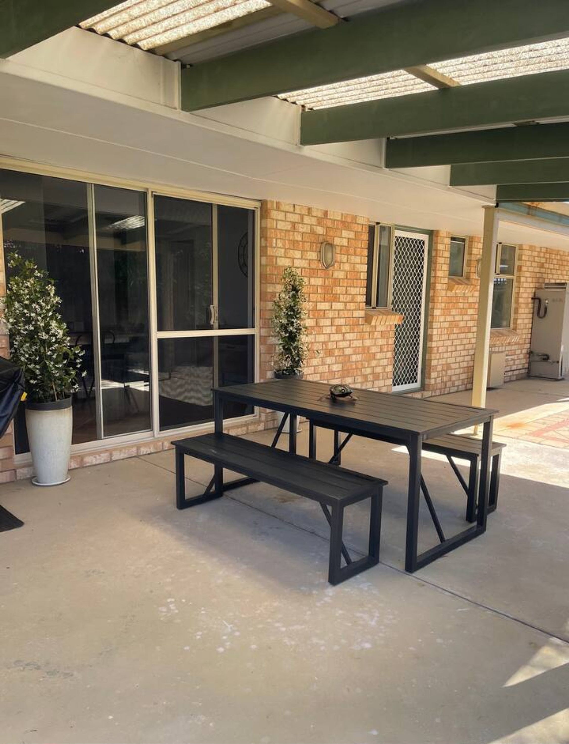 An outdoor patio area with a picnic table and benches, a potted plant, and a building with a brick facade and large windows.