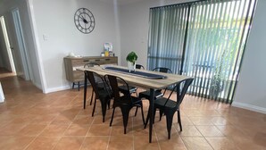 Un coin repas avec une table en bois, des chaises noires, une horloge au mur et une plante posée sur la table.