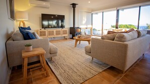 A modern living room with a sofa, a coffee table, a TV, and a fireplace. - West Beach Holiday Home (Esperance)