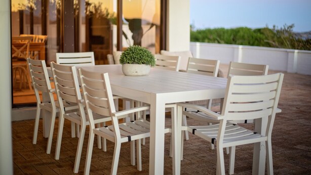 A white outdoor dining area with a table and chairs, a potted plant, and a view of greenery. - West Beach Holiday Home (Esperance)
