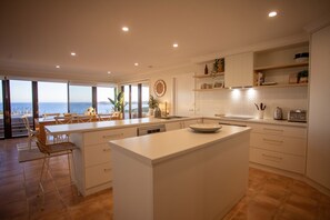A modern kitchen with a large island, white cabinetry, and a view of the sea.