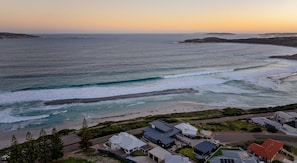 A coastal view with a beach, ocean waves, and a row of houses. - West Beach Holiday Home (Esperance)