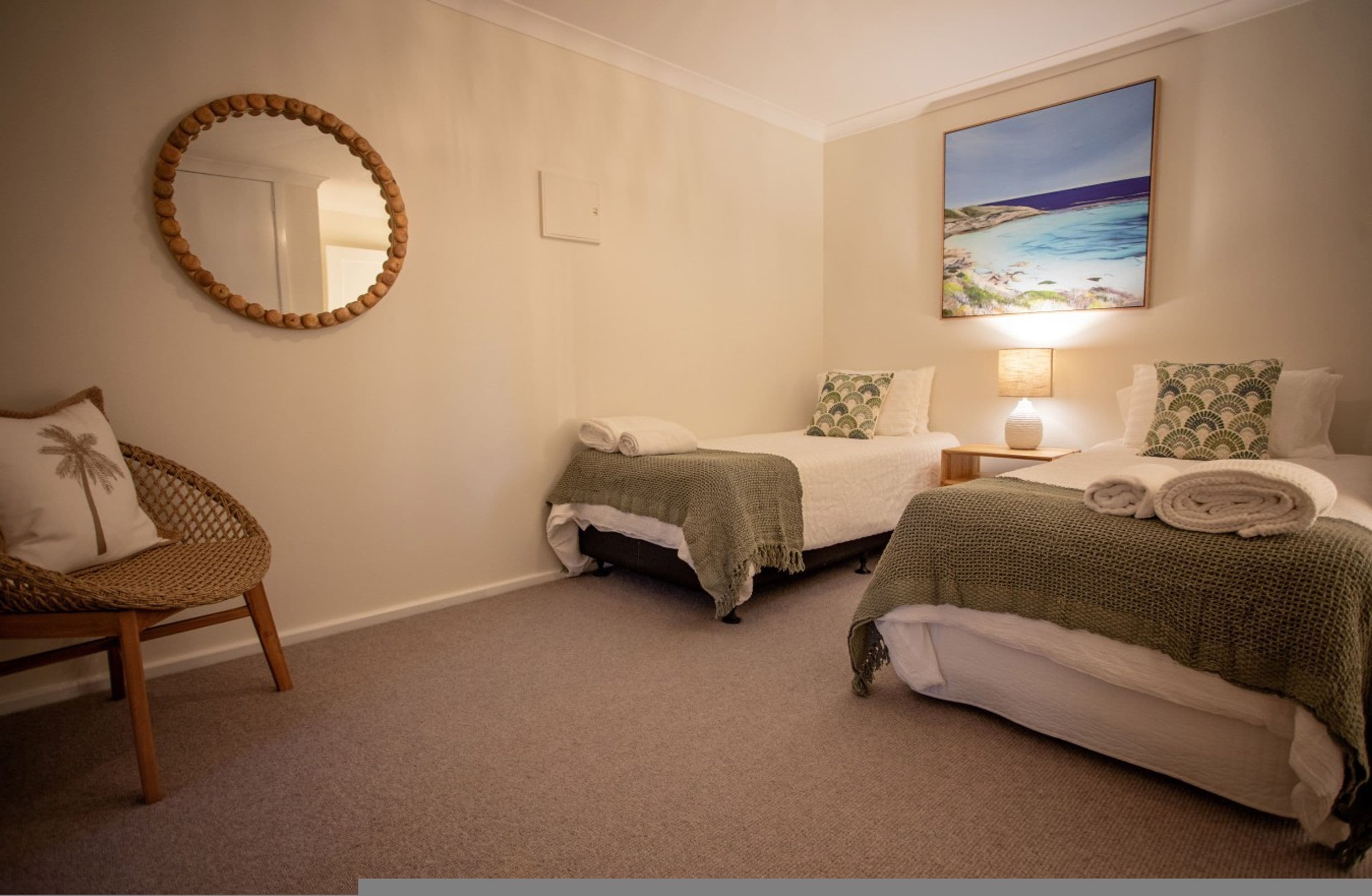 A bedroom with two beds, a chair, a painting, and a mirror.