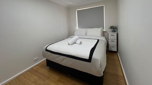 A modern hotel room with a bed, bedside table, and a nightstand with a plant. - Little Emily in Esperance (Esperance)