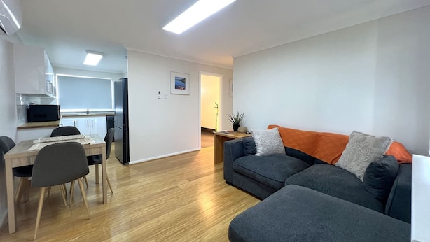 A modern living room with a sofa and ottoman, a dining area with a table and chairs, and a kitchen area with cabinets and appliances. - Little Emily in Esperance (Esperance)