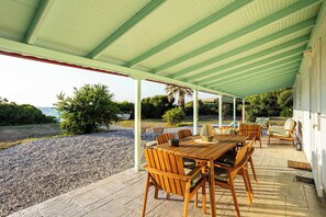 A covered outdoor dining area with a table and chairs, a view of the sea, and a gravel path. - Charming Beachfront Haven, Steps from the Beach (Kiparissia)