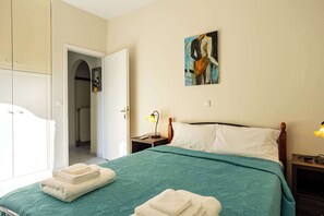 Een slaapkamer met een bed, nachtkastje, bedlamp, schilderij en een kledingkast.