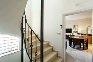 A staircase with a black metal railing leading to a kitchen area with a dining table and chairs. - Kyparissia Modern Home, Serene Views - Calm Vibes (Kiparissia)