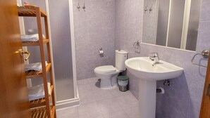 Ein Badezimmer mit Dusche, Toilette, Waschbecken und einem Holzregal mit Handtüchern.