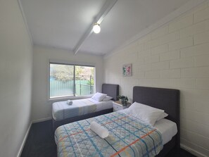 A bedroom with two beds, a window with a view, a light fixture, and a wall-mounted decoration.