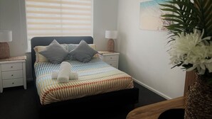 A bedroom with a bed, bedside tables, a lamp, a wall-mounted painting, and a potted plant.