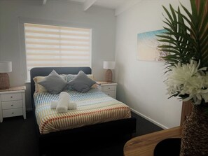 A bedroom with a bed, bedside tables, a lamp, a wall-mounted painting, and a potted plant.