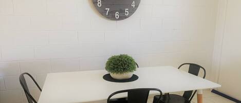 A dining area with a white table, two black chairs, and a round wall clock.