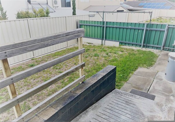 A fenced outdoor area with a wooden bench, a concrete pathway, and a green fence in the background.