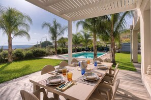 Un espace extérieur aménagé pour les repas, avec une piscine, des palmiers et une vue sur le paysage.