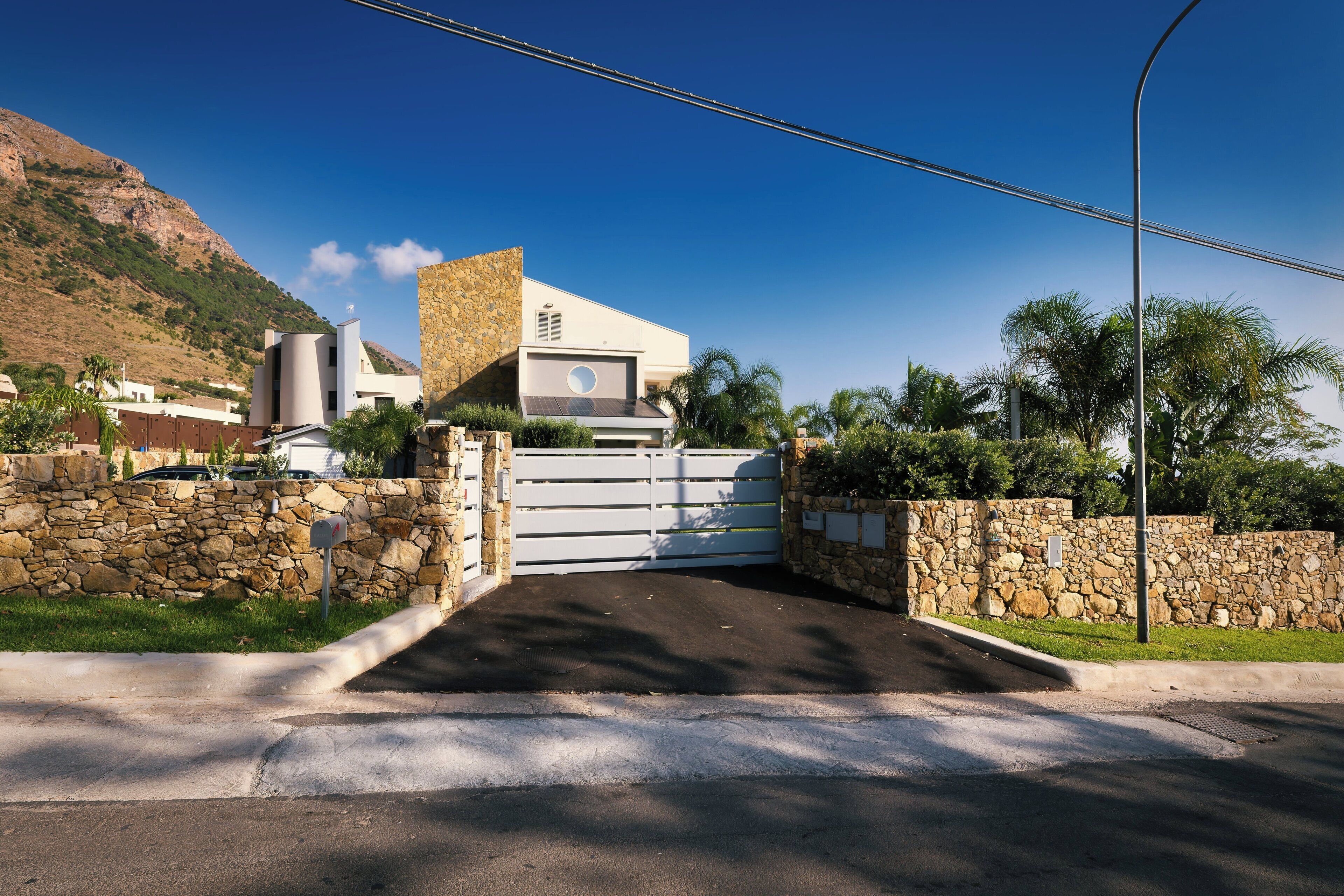 A gated entrance to a property with a stone wall and a modern building with a flat roof.