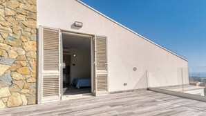 Ein modernes Gebäude mit einer Steinfassade, einem Balkon mit Holzboden und einem Schlafzimmer mit Bett und blauer Bettdecke.