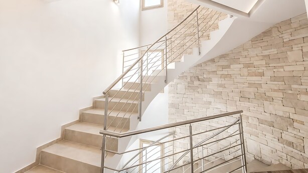 Eine moderne Treppe mit Metallgeländer, die zu einem Zwischenpodest mit einer Steinwand führt.