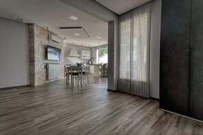 A modern kitchen with a stone wall, a dining area with a table and chairs, and a large window with curtains. - Villa Skyline: Design, Pool, Ocean View by Sicily Home Solutions (Castellammare del Golfo)