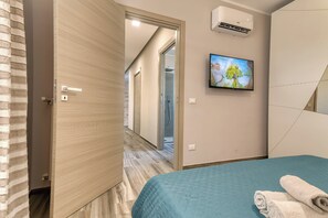 A hotel room with a bed, a television, an air conditioning unit, and a bathroom with a shower. - Villa Skyline: Design, Pool, Ocean View by Sicily Home Solutions (Castellammare del Golfo)