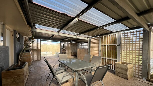 Eine überdachte Terrasse mit Tisch, Stühlen, einem Grill und einem Blumentopf.