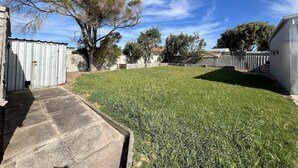 Ein Garten mit Rasen, einem Betonweg, einem Metallschuppen und einem weißen Gebäude.