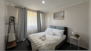 Ein Schlafzimmer mit Bett, Nachttisch, Kleiderhaken und einem Fenster mit Vorhängen.