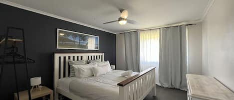 A bedroom with a bed, a ceiling fan, a nightstand, a chair, and a window with curtains.