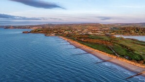Un paisaje costero con playa, un pueblo a lo lejos y una masa de agua.