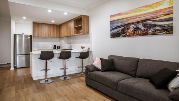 A modern kitchen with a refrigerator, wooden cabinets, and a bar area with stools. - Seabreeze Esperance in West Beach (Esperance)