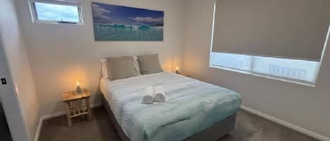 A bedroom with a bed, a nightstand, a painting, and a window.