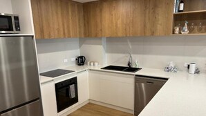 A modern kitchen with white cabinetry, stainless steel appliances, and a wooden upper section. - Seabreeze Esperance in West Beach (Esperance)